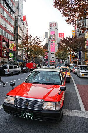 Taxi rossi su strada trafficata davanti a Shibuya 109 a Tokyo, Giappone.