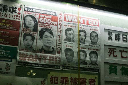 Manifesti della polizia giapponese con foto di persone ricercate affissi dietro una vetrata in un luogo pubblico.
