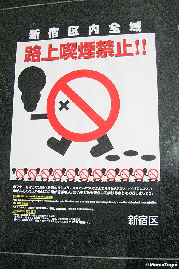 Cartello informativo con divieto fumo shinjuku affisso a terra su una superficie scura in Giappone.