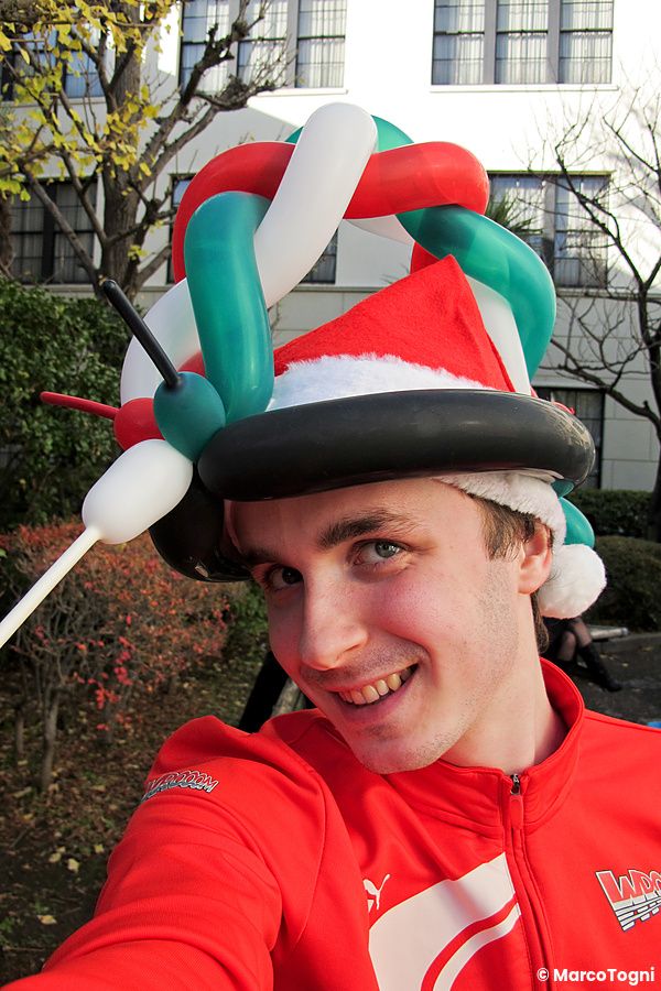 Marco Togni con cappello di palloncini e cappello di Babbo Natale sorridente all'aperto.