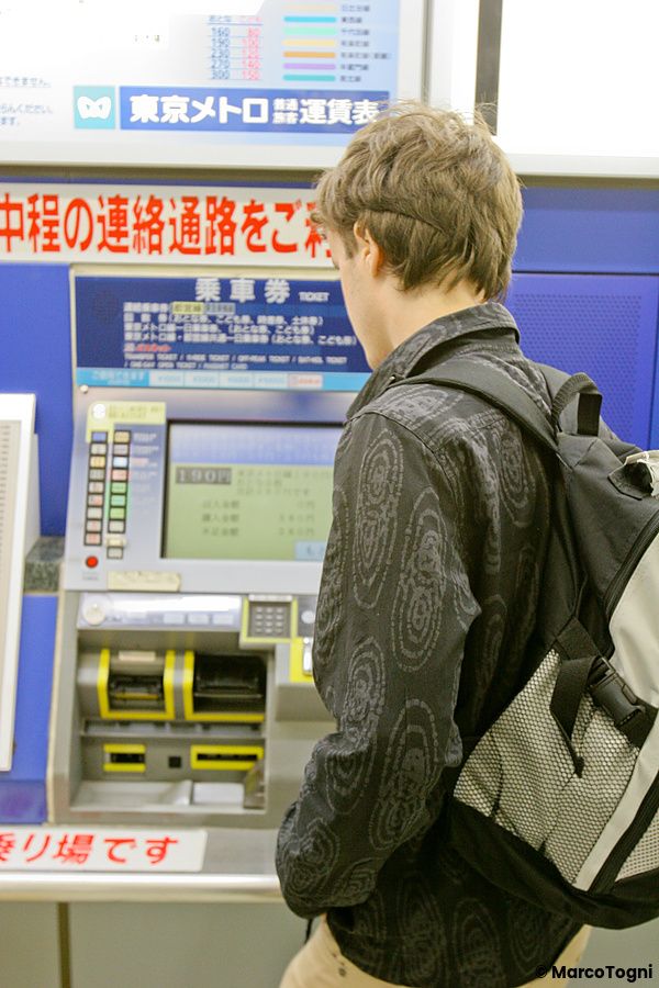 Un uomo con uno zaino sta acquistando un biglietto presso una macchinetta automatica in una stazione a Tokyo.