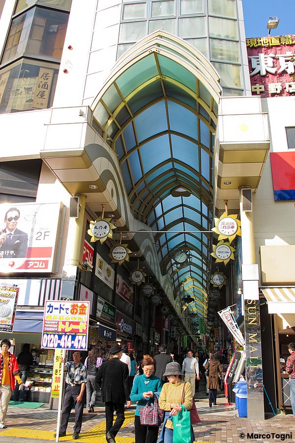 Ingresso del Nakano Broadway a in Giappone con una copertura ad arco in vetro e persone che camminano nel corridoio.