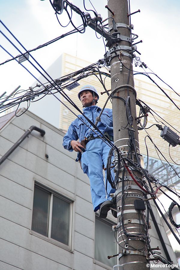 Operaio giapponese su un palo della luce circondato da cavi elettrici.