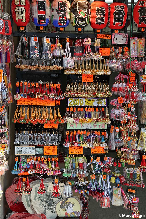 Una parete di un negozio in Nakamise Dori ricoperta di portachiavi e gadget appesi con lanterne decorate in alto.