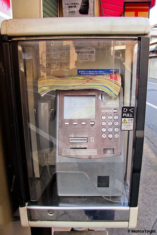 Un telefono pubblico giappone NTT all'interno di una cabina trasparente posizionato lungo una strada in Giappone.