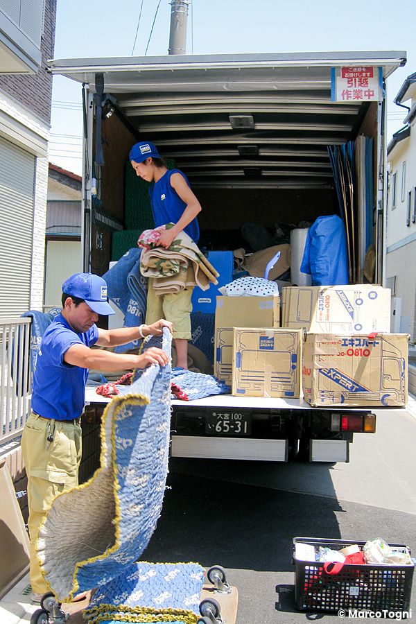 Due persone sistemano scatoloni in un camion per trasloco in una strada giapponese.