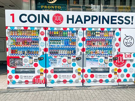 Tre distributori automatici di bevande colorati con scritte promozionali in un'area urbana a Shimbashi.