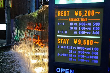 Ingresso di un love hotel in Giappone con cartello delle tariffe e cascata.