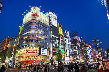 Strada affollata a Shinjuku, Tokyo, con insegne al neon e persone.