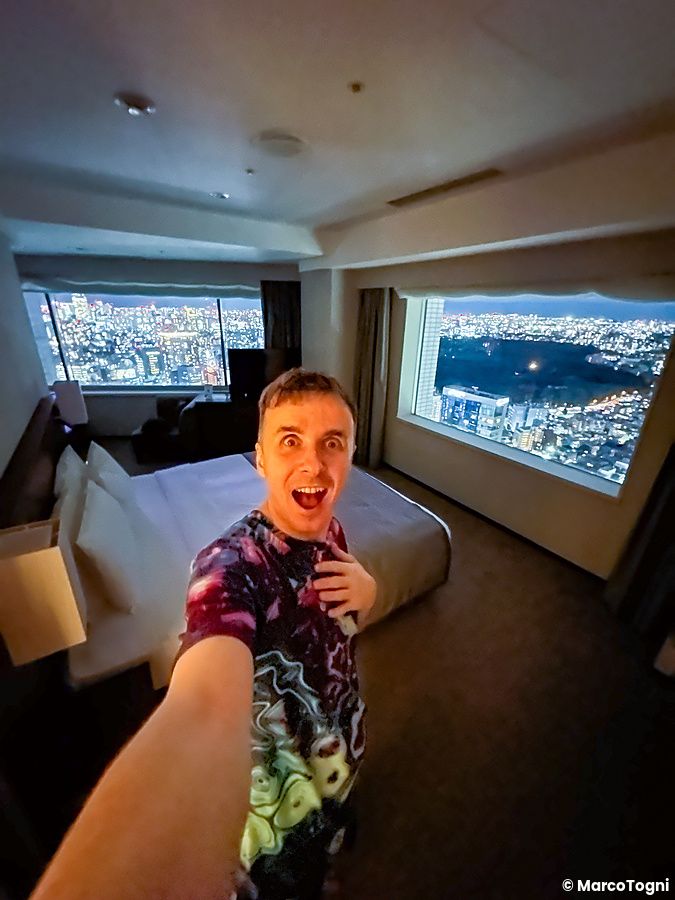 Marco Togni in una camera d'hotel con vista notturna su Tokyo.