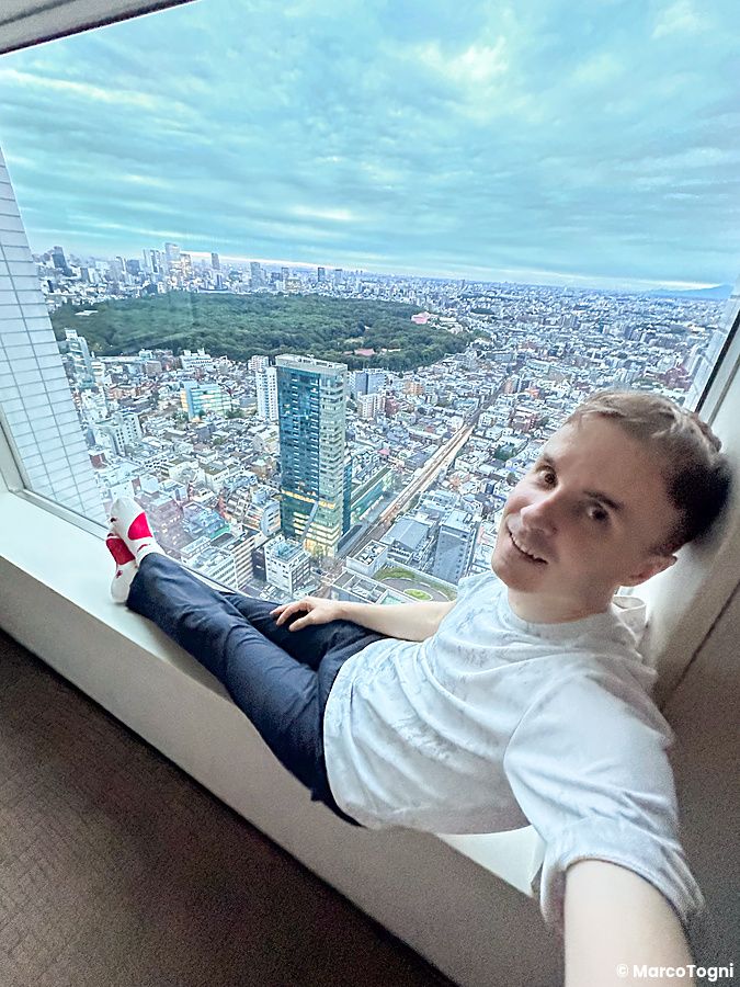 Marco Togni seduto vicino a una finestra con vista su Tokyo da un hotel.