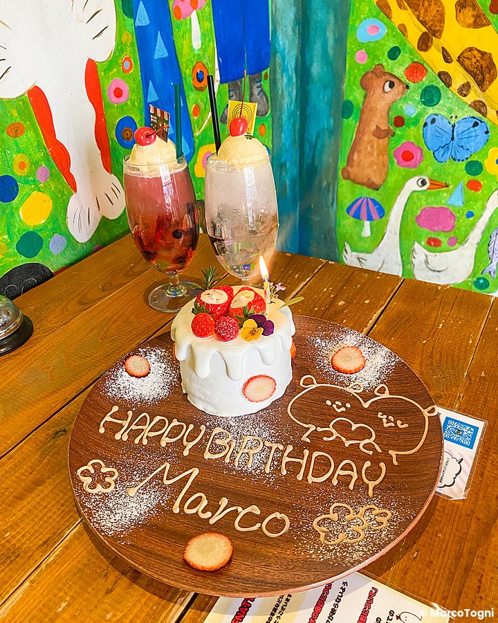 Un piatto di buon compleanno a Hattifnatt con una piccola torta bianca e scritte di auguri su un vassoio di legno.