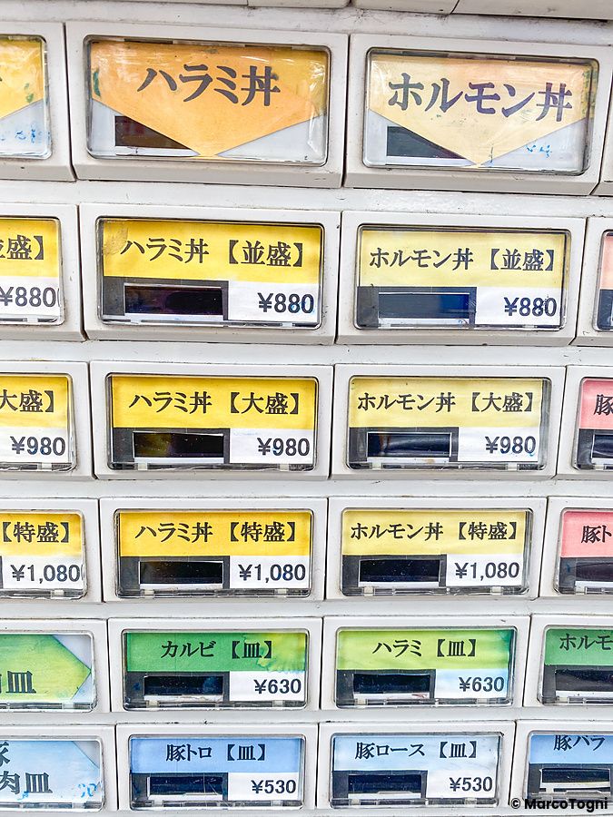 Pannello di un distributore automatico di biglietti per cibo con scritte in giapponese e prezzi a Shimbashi.
