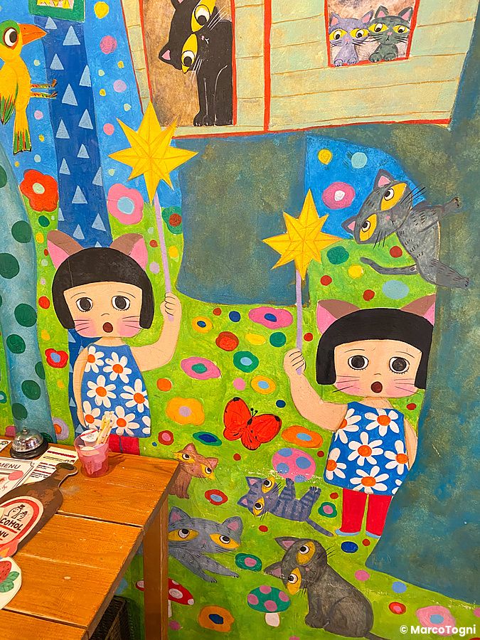 Un murale colorato all'interno del ristorante Hattifnatt a Kichijoji raffigura bambine e gatti in stile illustrato.