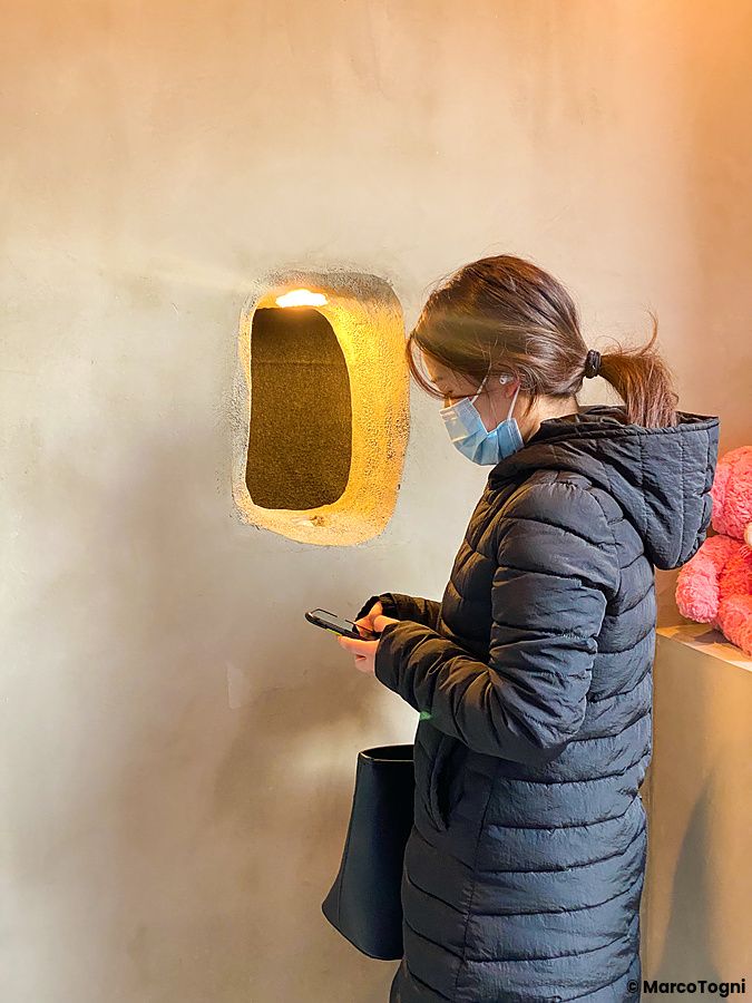 Una donna con mascherina osserva il telefono vicino all'apertura nel muro del Kuma no Te Cafe, Osaka.