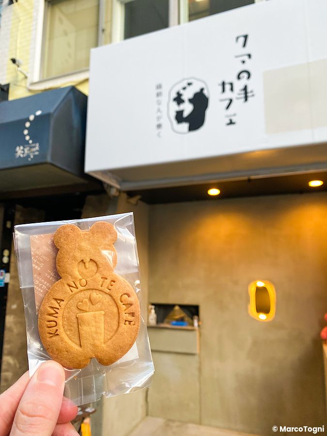 Un biscotto a forma di orso tenuto in mano davanti all'ingresso del Kuma no Te Cafe, Osaka.