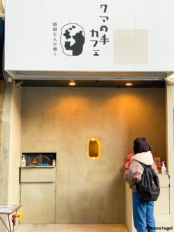 Una persona in attesa davanti al Kuma no Te Cafe, Osaka, dove un foro nel muro permette il servizio delle bevande.