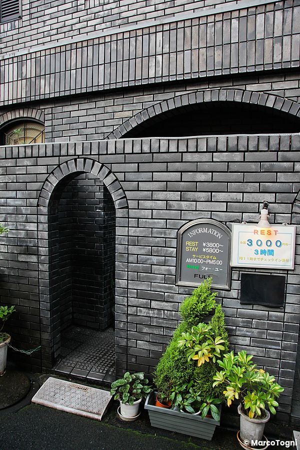 Ingresso di un love hotel in Giappone con mattoni scuri e piante decorative.