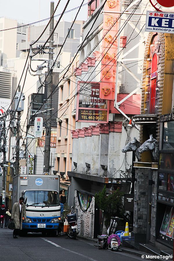 Strada urbana in Giappone con love hotel e traffico.