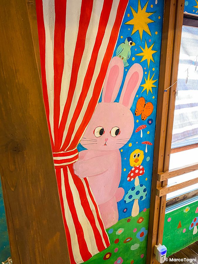 Un murale colorato all'interno del ristorante Hattifnatt mostra un coniglio rosa che tiene una tenda a righe rosse.