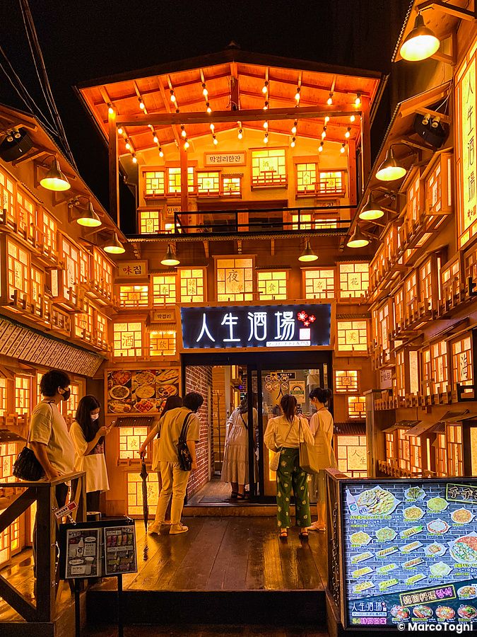 L'ingresso di un ristorante coreano a Shin Okubo illuminato da calde luci, con persone in piedi davanti alla porta.