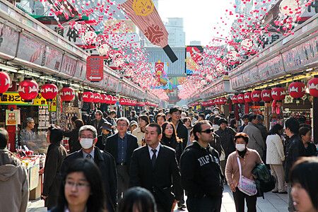 Molte persone camminano lungo la via commerciale Nakamise-dori ad Asakusa sotto file di lanterne rosse e decorazioni.