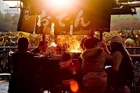 Persone riunite attorno a un chiosco di oden al tramonto nel parco di Ueno, Tokyo.