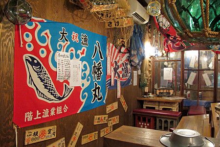 Interno di un izakaya giapponese con decorazioni a tema pesca e tavoli in legno.