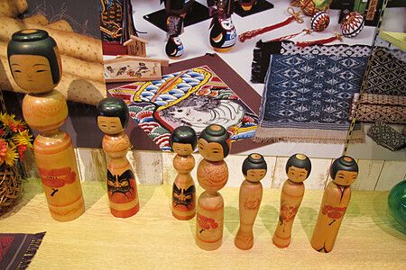 Bambole kokeshi giapponesi su un tavolo con sfondo di tessuti tradizionali.