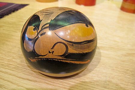 Bambola kokeshi sferica dipinta con volto stilizzato.