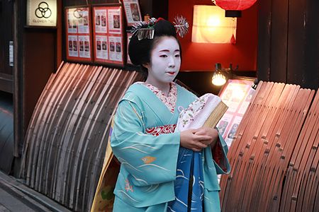 Una giovane maiko in kimono azzurro cammina in un vicolo tradizionale di Kyoto.