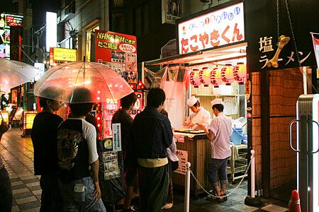 Persone in fila davanti a un chiosco di takoyaki a Osaka di notte.