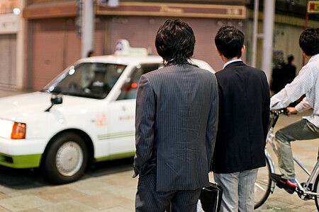 Due uomini in abiti formali aspettano un taxi in Giappone.