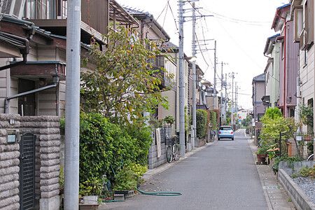 Strada residenziale tranquilla a Shinden con case, alberi e automobili parcheggiate.