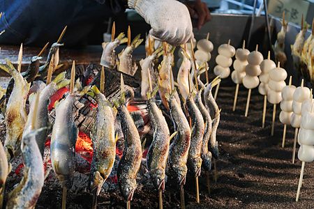 Pesci e dango su spiedini in cottura su barbecue in Giappone.