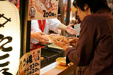 Una persona prende un piatto di takoyaki da una bancarella a Osaka.
