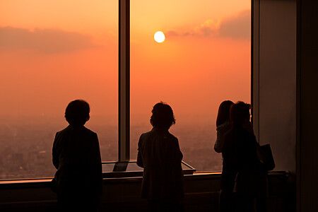 Persone osservano il tramonto attraverso una grande vetrata.