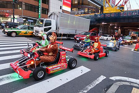 Persone in go-kart con costumi attraversano un incrocio a Tokyo.