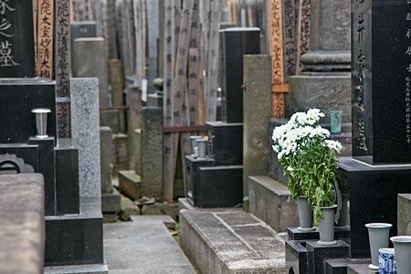 Un mazzo di fiori bianchi posato su una tomba nel cimitero di Yanaka a Tokyo, circondato da lapidi in pietra.