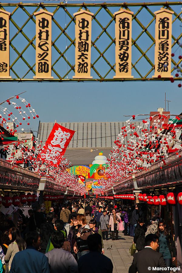 Una folla di persone cammina lungo la via Nakamise ad Asakusa sotto file di decorazioni sferiche rosse e bianche.