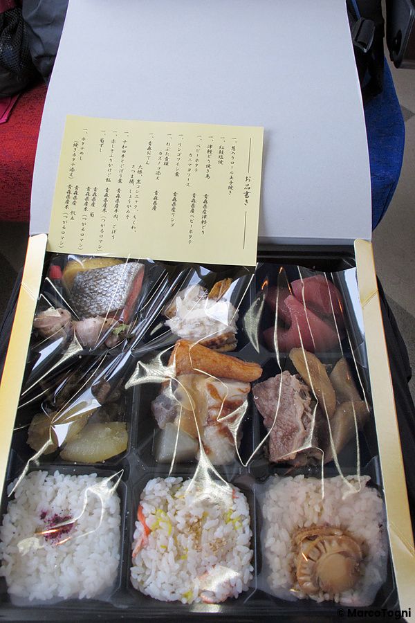 Ekiben aperto con cibi assortiti e foglio descrittivo su un treno in Giappone.