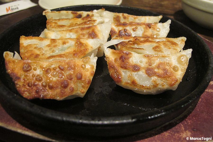 Gyoza dorati su piatto nero in un izakaya giapponese.