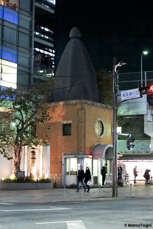 Un edificio in mattoni con una cupola scura, identificato come un koban, di notte in una strada urbana di Tokyo.