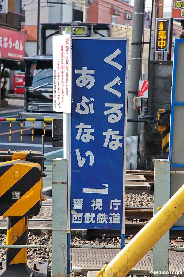 Cartello blu di avvertimento presso un passaggio a livello ferroviario nei luoghi di Maison Ikkoku in Giappone.