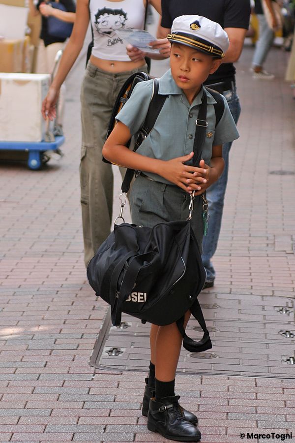 Bambino in divisa scolastica giapponese con cappello bianco cammina su un marciapiede