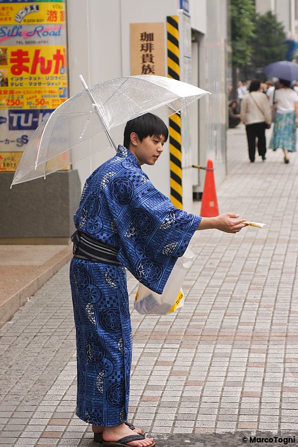Una persona in yukata distribuisce volantini su un marciapiede in Giappone