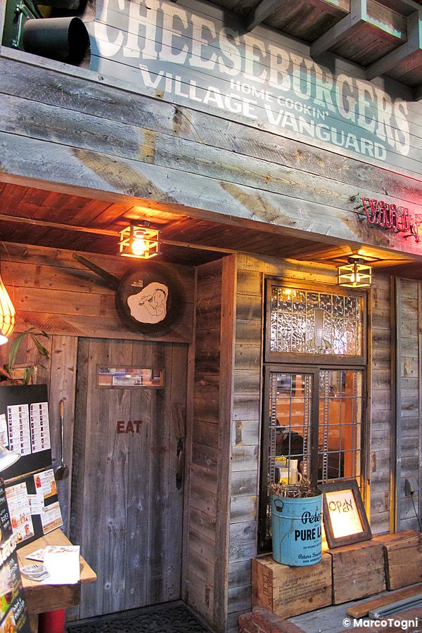 Ingresso rustico in legno del Ristorante di cheeseburger Village Vanguard con insegna in rilievo e decorazioni vintage.
