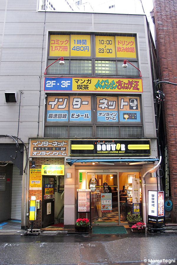 Facciata di un edificio in Giappone con insegna del caffe doutor giappone al piano terra e cartelli di internet café.