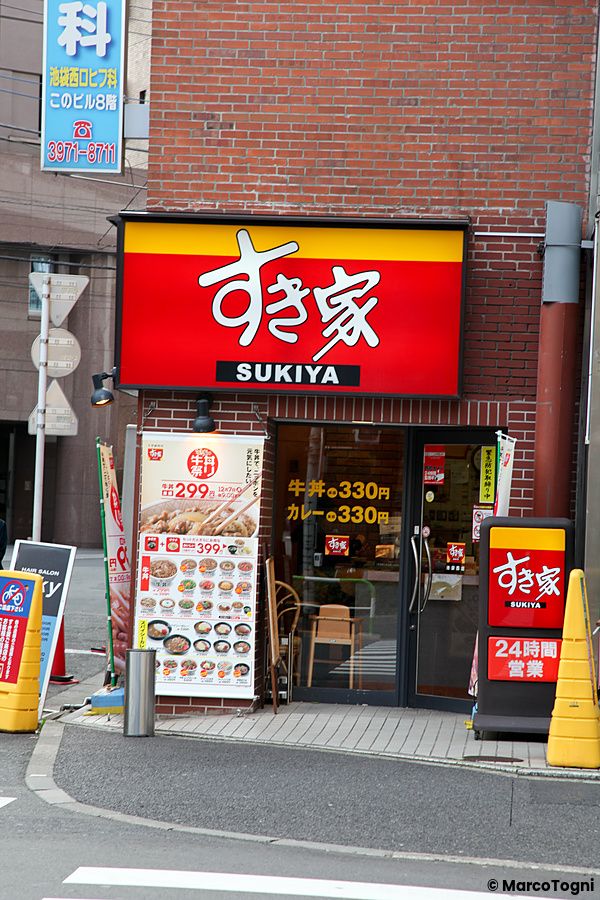 Ingresso di un ristorante Sukiya in Giappone con insegna rossa e menu esterno.