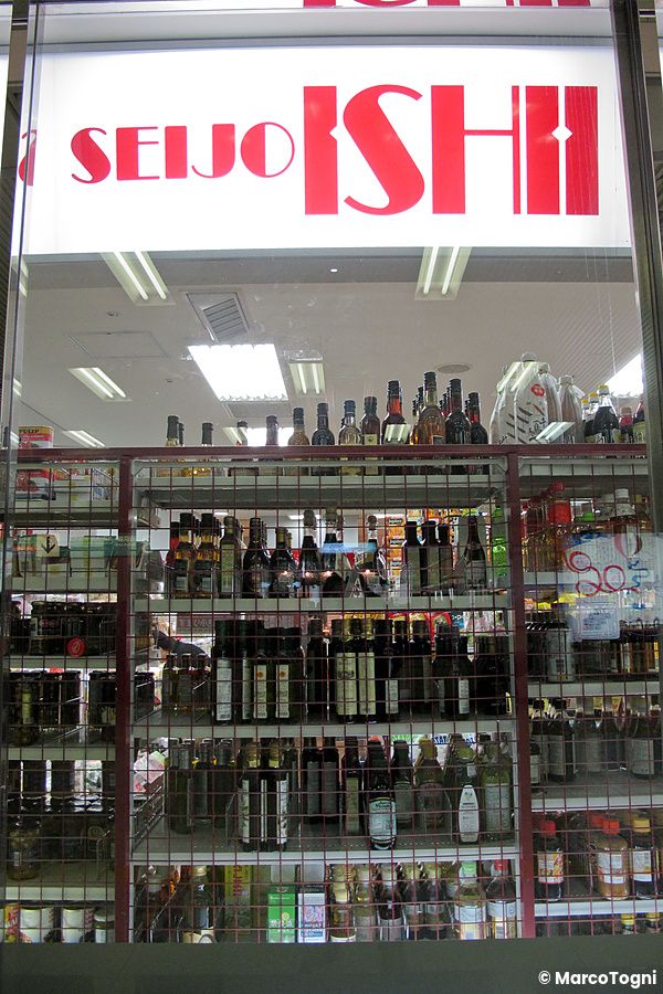 La vetrina del negozio Seijo Ishii con scaffali colmi di bottiglie di olio e condimenti visibili dietro il vetro.